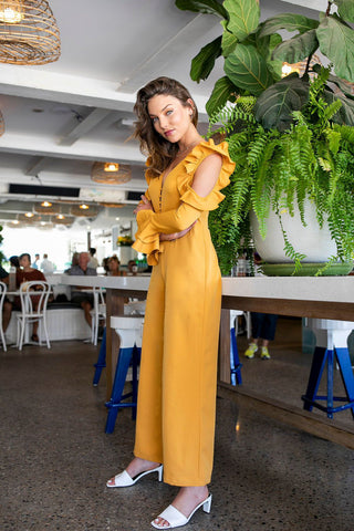 Side view of the jumpsuit in a cafe showing off the standout cut-out sleeve with ruffle detail.