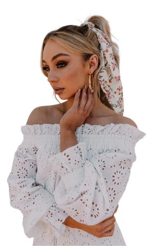 Close up view of white eyelet off the shoulder jumpsuit with ruffle neckline and ruffle sleeve.