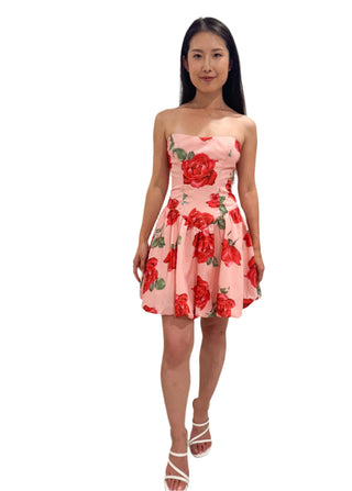 Model wearing strapless mini dress with rose print and styled with white heel.