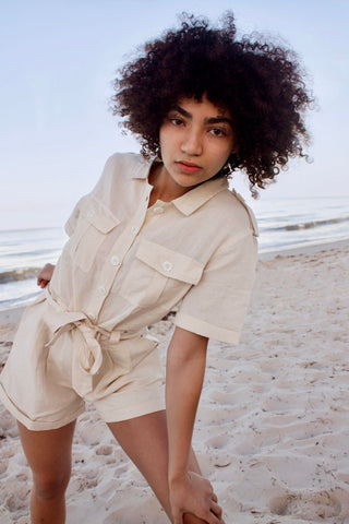Model on beach wearing safari style button up playsuit with waist tie.