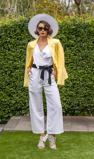White jumpsuit styled with black belt, yellow blazer and white heels and hat.