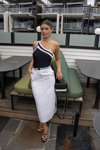 Model wearing high waisted pinstripe linen midi skirt with fitted one shoulder black top and black heels.