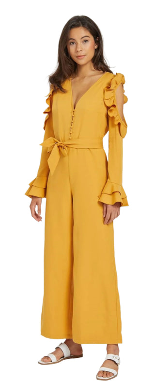 Side view of mustard jumpsuit with cut out long sleeve with ruffles.