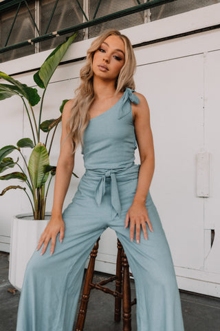 Model sitting down in blue linen pantsuit with tie sholder and tie waist.