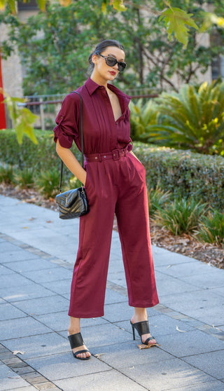 Model wearing burgundy jumpsuit styled with black accessories.