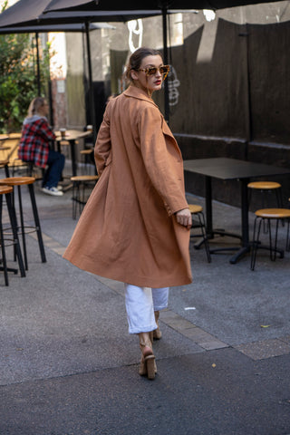 Back view of long line brown jacket with whtie jeans, heels and sunnies.