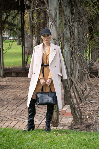 Cream coat styled edgy with black boots, bag and cap.