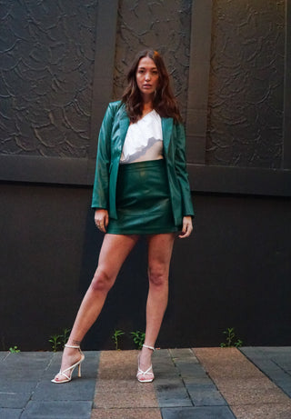 Woman in a green blazer and skirt standing against a textured wall.