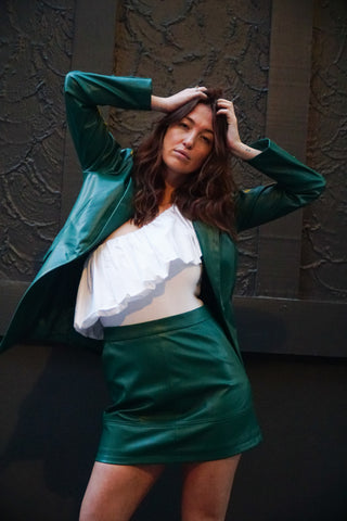 Model styling the matching vegan leather skirt and blazer set with a ruffle one shoulder white bodysuit.